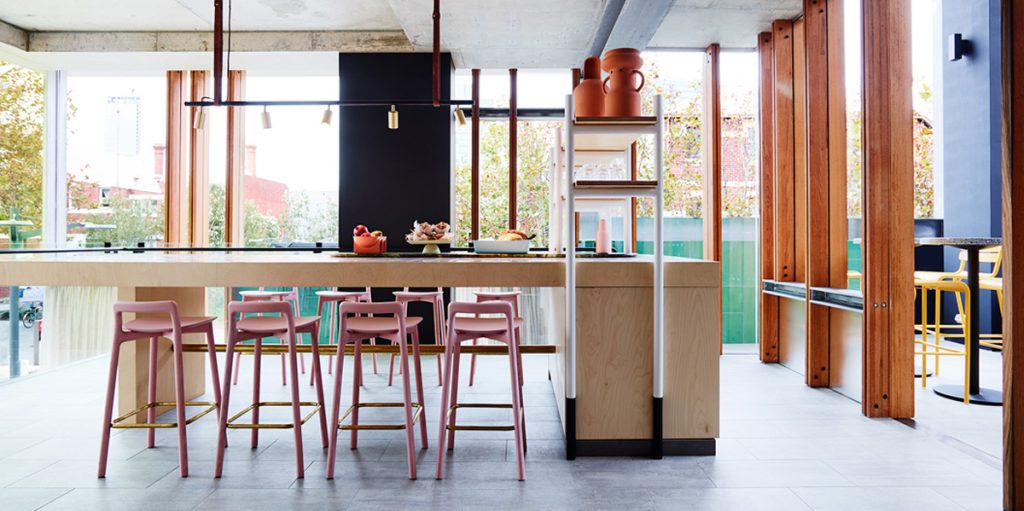 Commercial kitchen and bar with pink stools and timber columns by Arent & Pyke