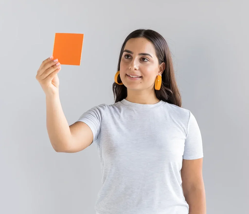Student holding up an orange colour swatch against a grey wall